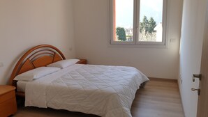A bedroom with a bed, a nightstand, a window, and a door. - Modern apartment in Porlezza (Porlezza)