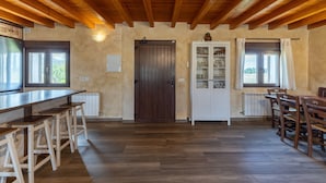 A kitchen with wooden beams, a long counter, stools, a door, and a cabinet with glass doors. - Paraje Navazos – Rural House in Sierra de Gredos with Pool and Mountain Views (Gavilanes)