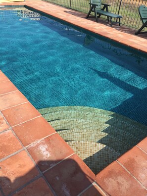 En swimmingpool med fliset kant og en patio med bænke.