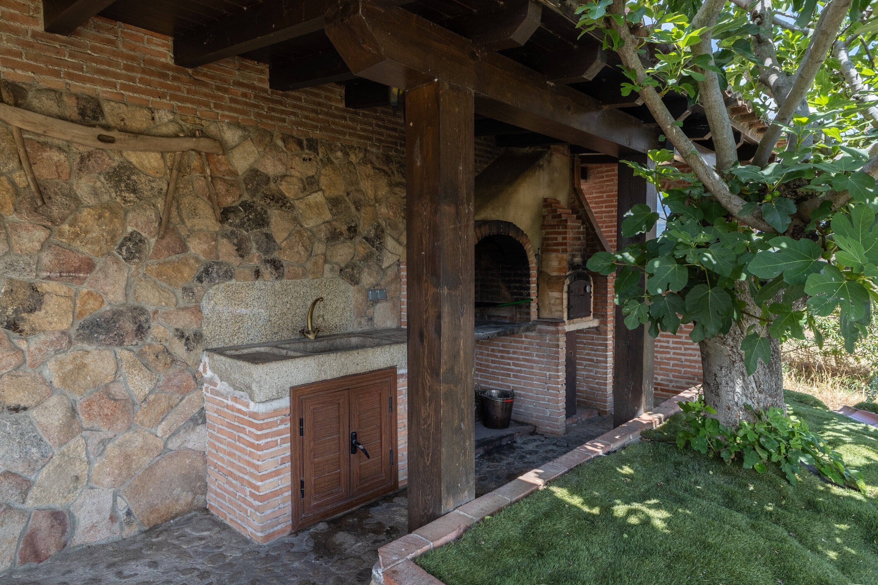 Un edificio de piedra con un horno de ladrillo, vigas de madera y un árbol de hojas verdes.