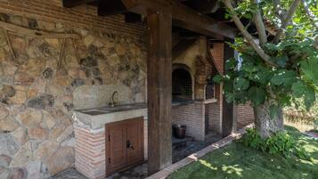 Un edificio de piedra con un horno de ladrillo, vigas de madera y un árbol de hojas verdes.