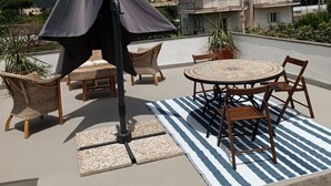 An outdoor patio with a round table and chairs, a striped rug, and a black umbrella. - Holiday Home 'Casetta Esmeralda' with Sea View, Private Terrace and Wi-Fi (Tortora Marina)