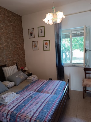 A bedroom with a bed, pillows, a nightstand, a lamp, a window with a view, and framed botanical prints on the wall. - Holiday Home 'Casetta Esmeralda' with Sea View, Private Terrace and Wi-Fi (Tortora Marina)