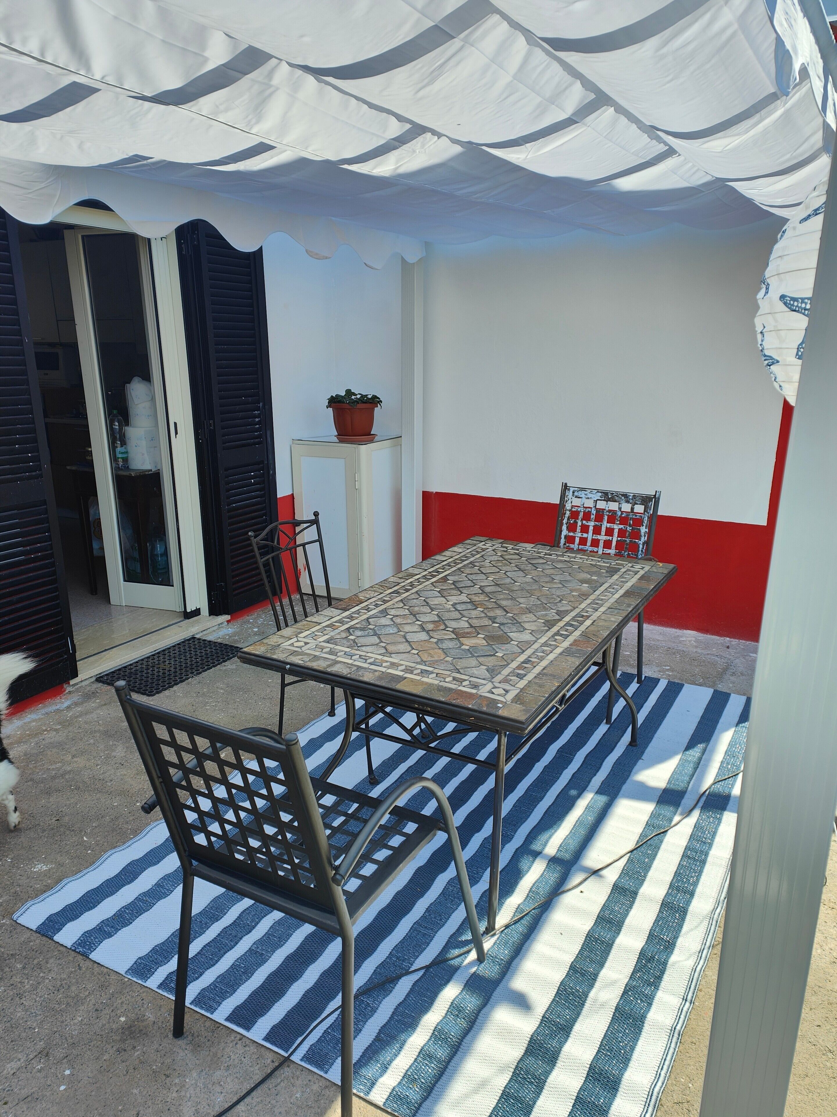 An outdoor patio with a tiled table and chairs, a striped rug, and a potted plant.