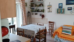 A room with a dining table, chairs, a bed, a shelf with decorative items, and a hanging light fixture. - Holiday Home 'Casetta Esmeralda' with Sea View, Private Terrace and Wi-Fi (Tortora Marina)