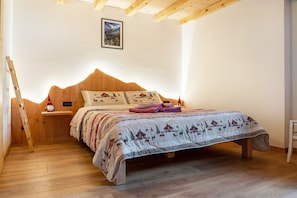 A bedroom with a wooden headboard, a bed with a patterned bedspread, a nightstand with a lamp, and a framed picture on the wall.
