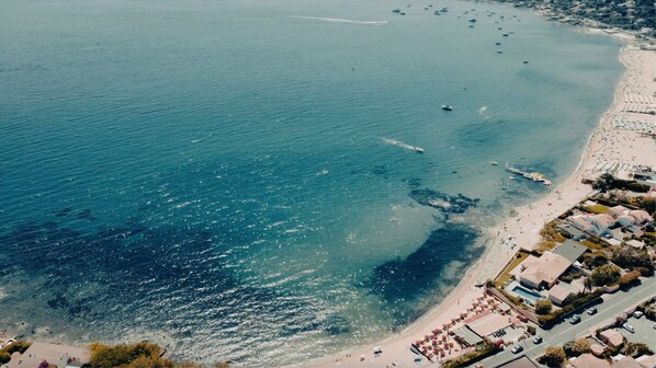 Vista aérea de una zona costera con playa, barcos y una hilera de edificios con piscina.