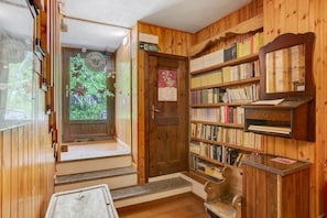 A wooden interior with a bookshelf, a door with a poster, and a window with a view of greenery. - Room “Potze” – Family Comfort (Saint Pierre)