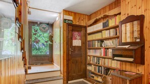 Een houten interieur met een boekenkast, een deur met een poster en een raam met uitzicht op groen.
