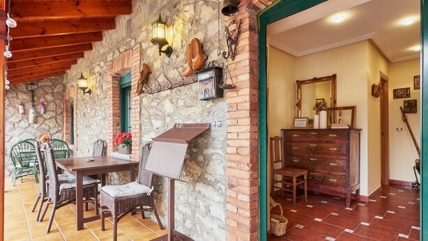Una habitación con paredes de piedra, una mesa de madera, sillas, un atril y un espejo en la pared.