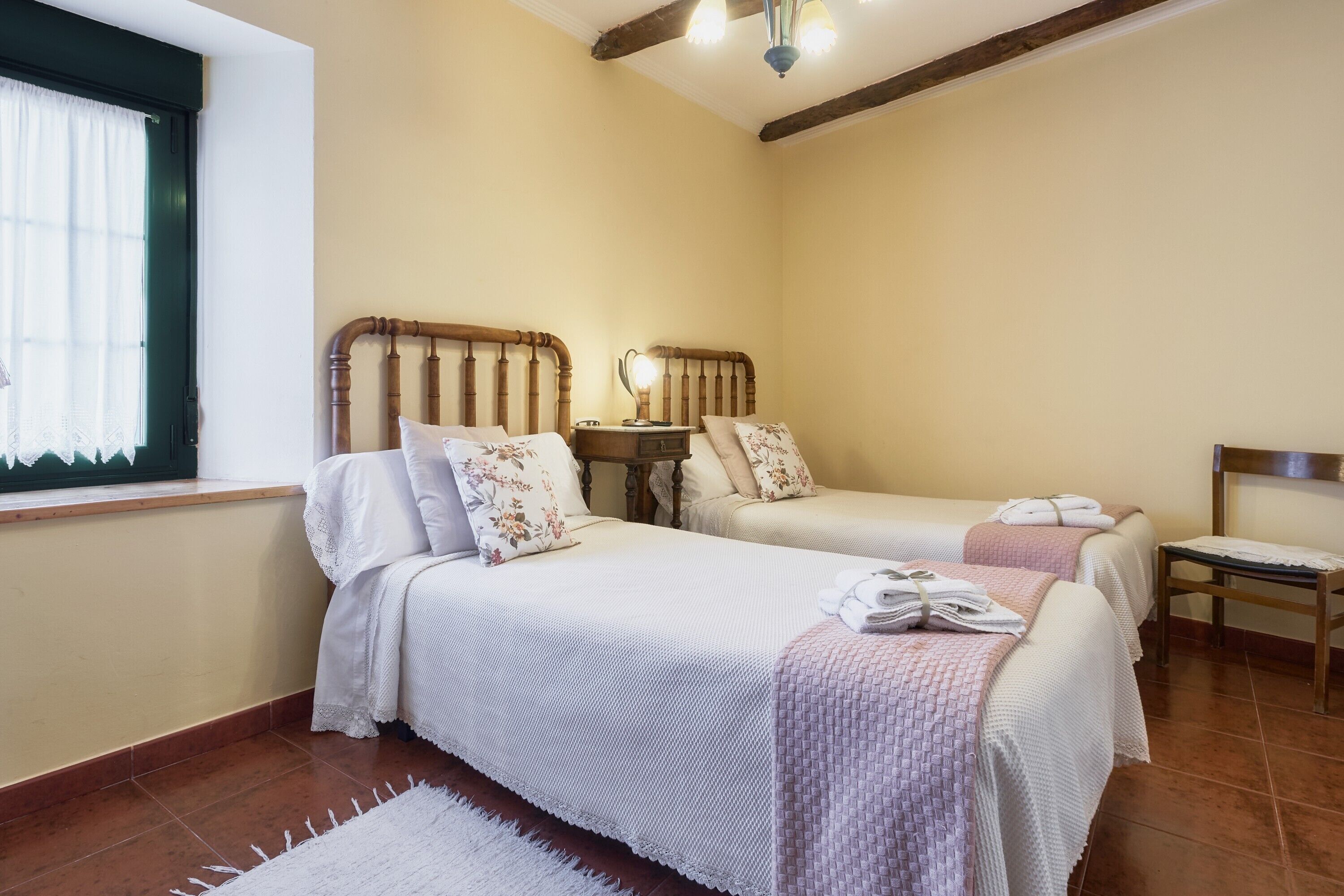 A bedroom with two beds, a small table, and a chair.