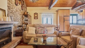 Una sala de estar acogedora con chimenea, un sofá, una mesa de centro de vidrio y una cocina al fondo.