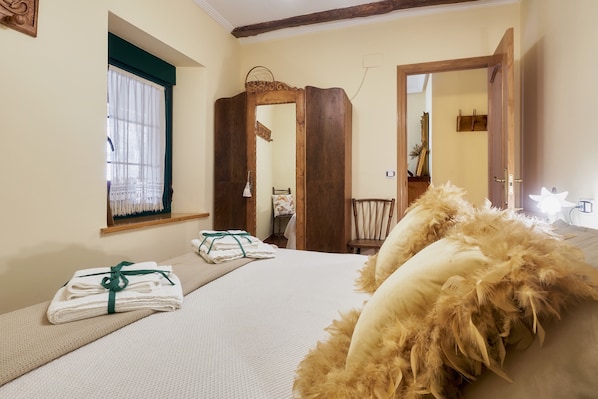 A bedroom with a bed, a window with curtains, a wooden door, and a mirror.