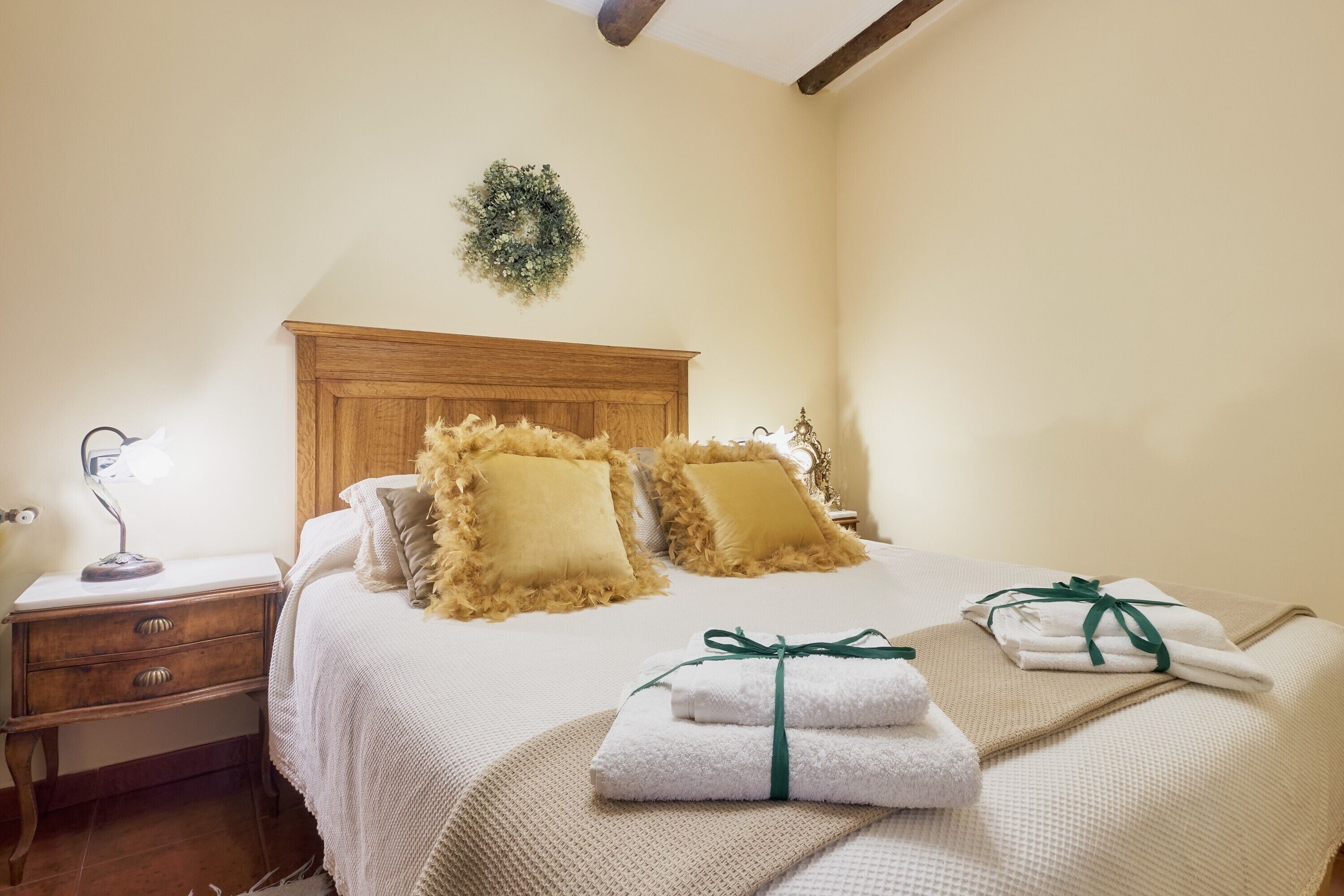 Una cama bien hecha con almohadas mullidas, una lámpara de noche y una mesita de madera.