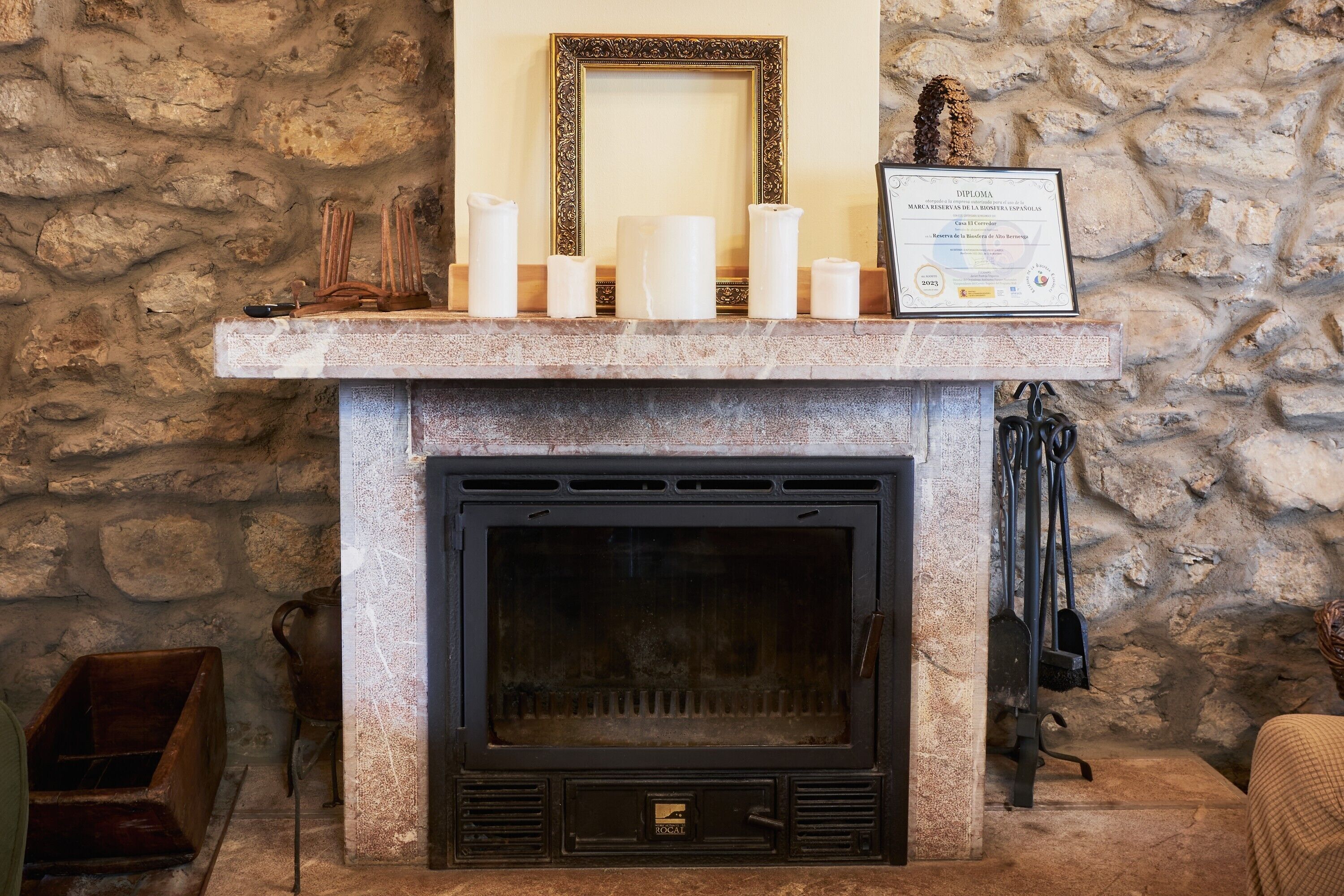 A stone wall, a fireplace with a framed diploma, and candles on a mantel.