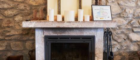 A stone wall, a fireplace with a framed diploma, and candles on a mantel.