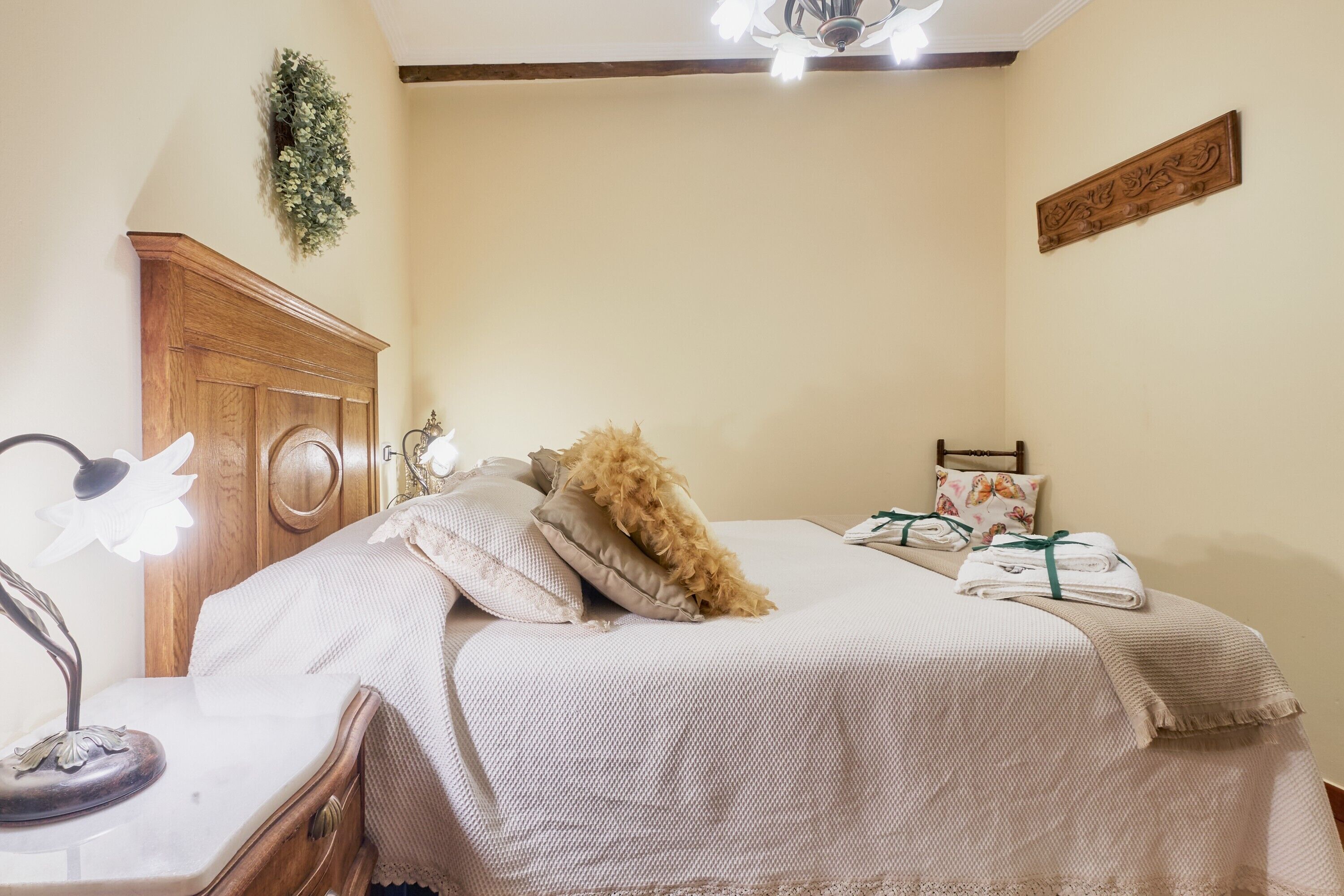 Een slaapkamer met een bed, nachtkastje, lamp, houten hoofdeinde en een decoratie aan de muur.