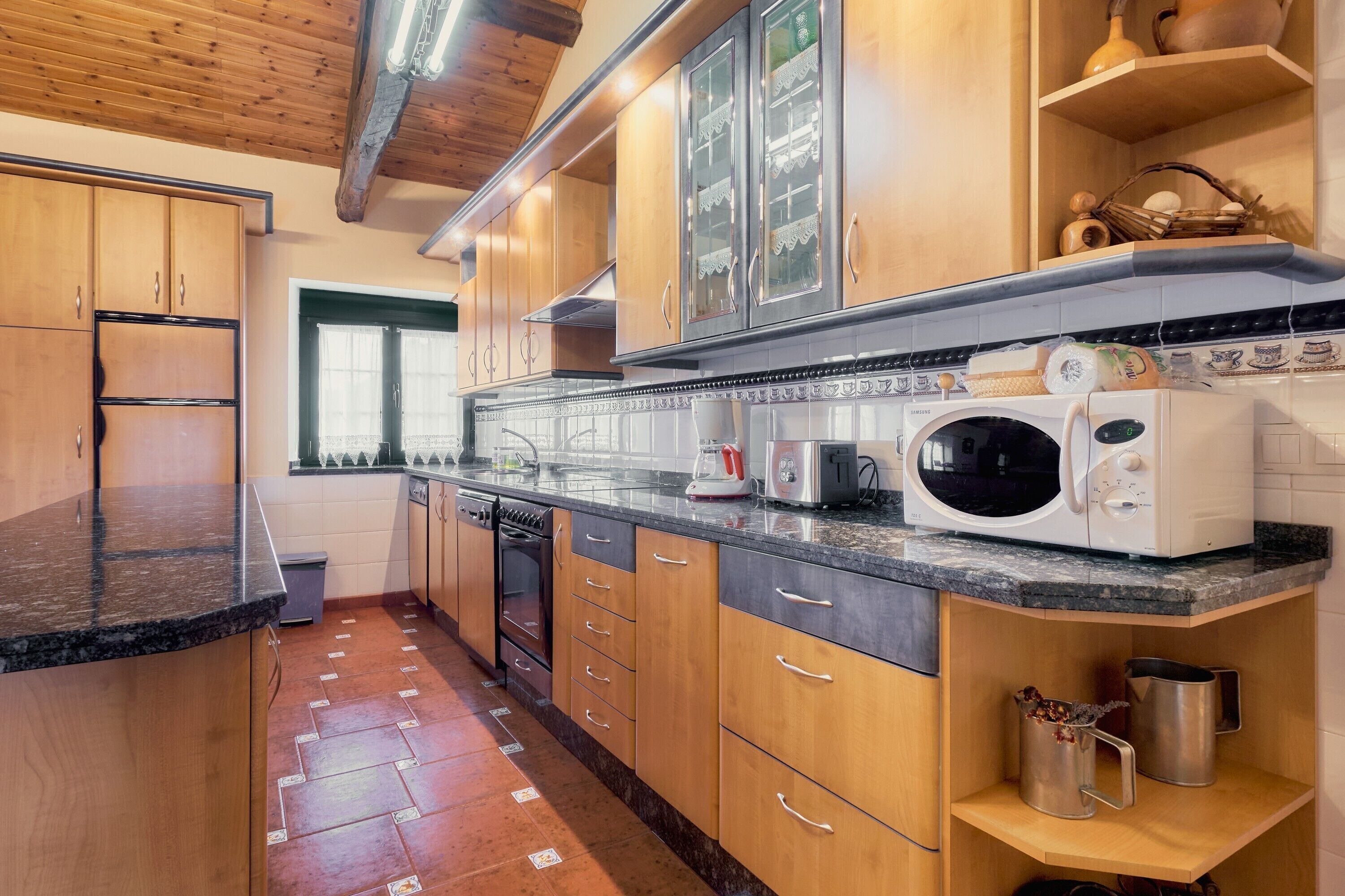 Una cucina con mobili in legno, un forno a microonde, un tostapane e una finestra con tende.