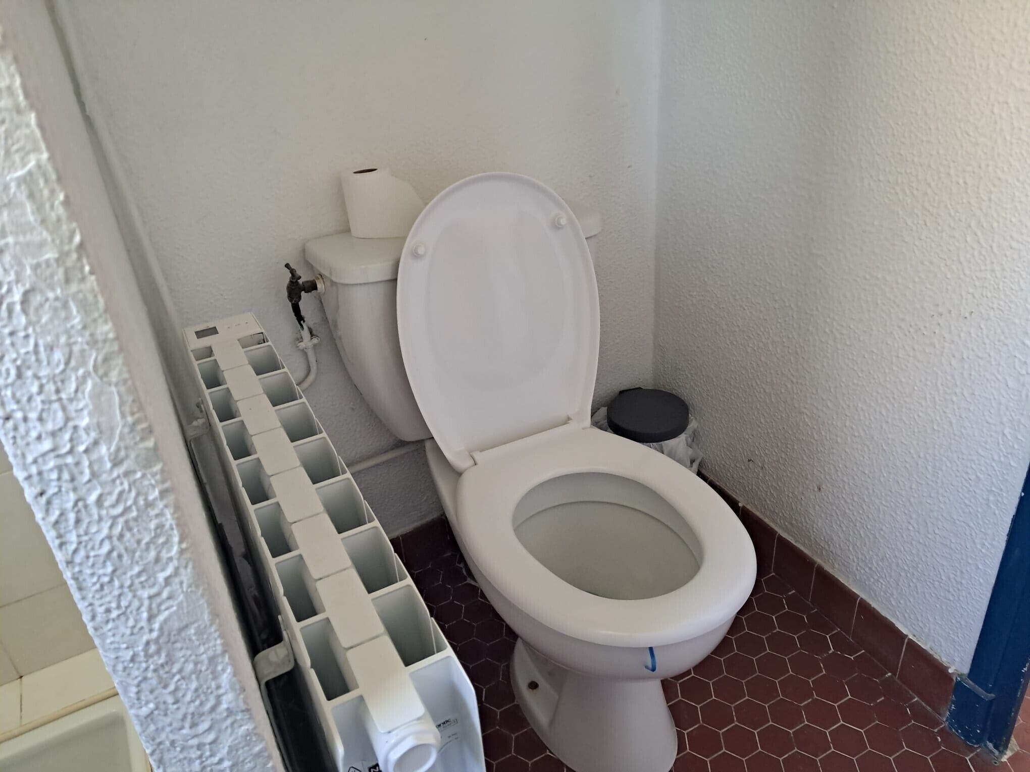 Een wit toilet met open deksel, een toiletrolhouder en een prullenbak.