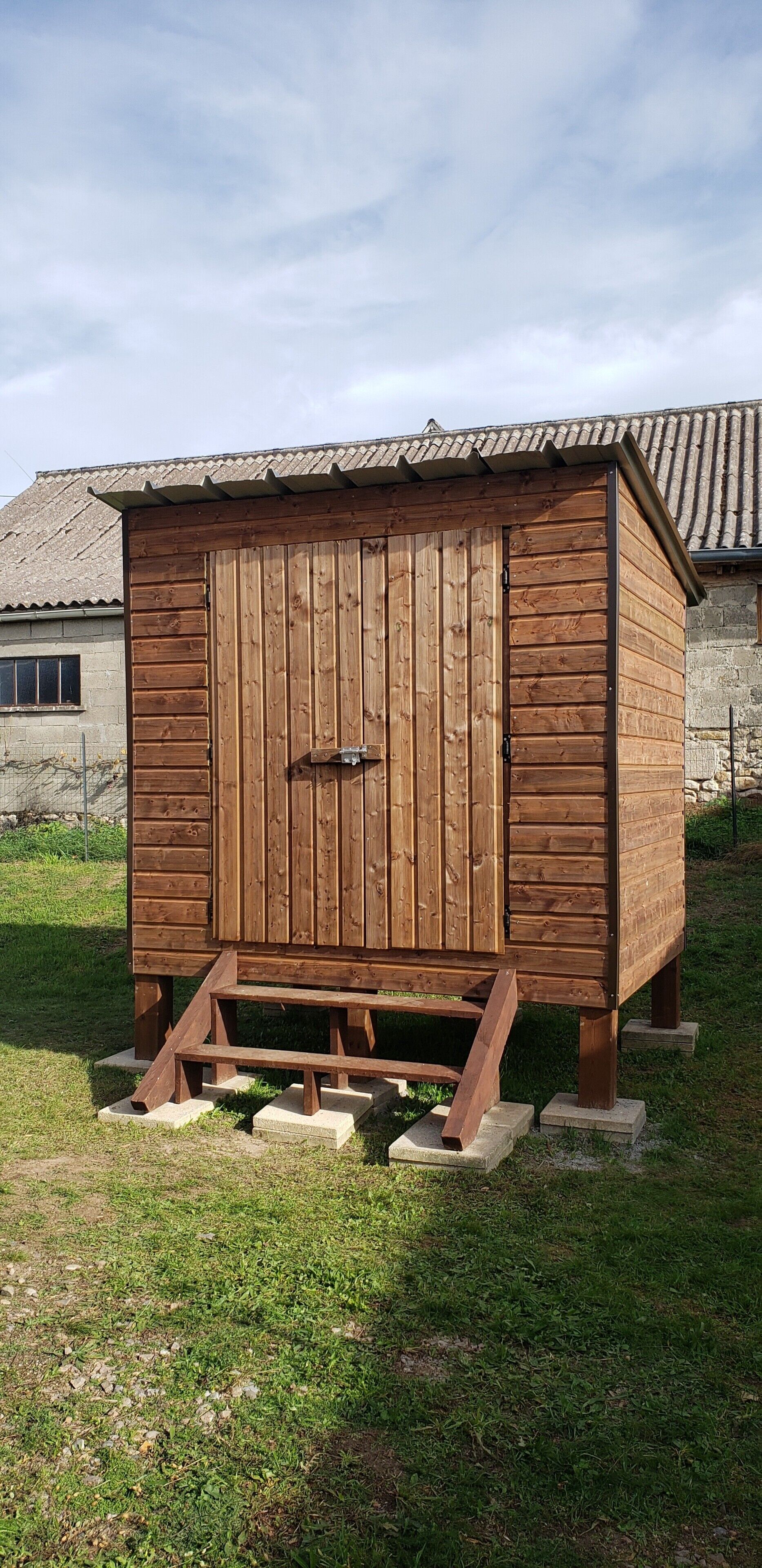 A wooden shed with a door, steps, and a roof.