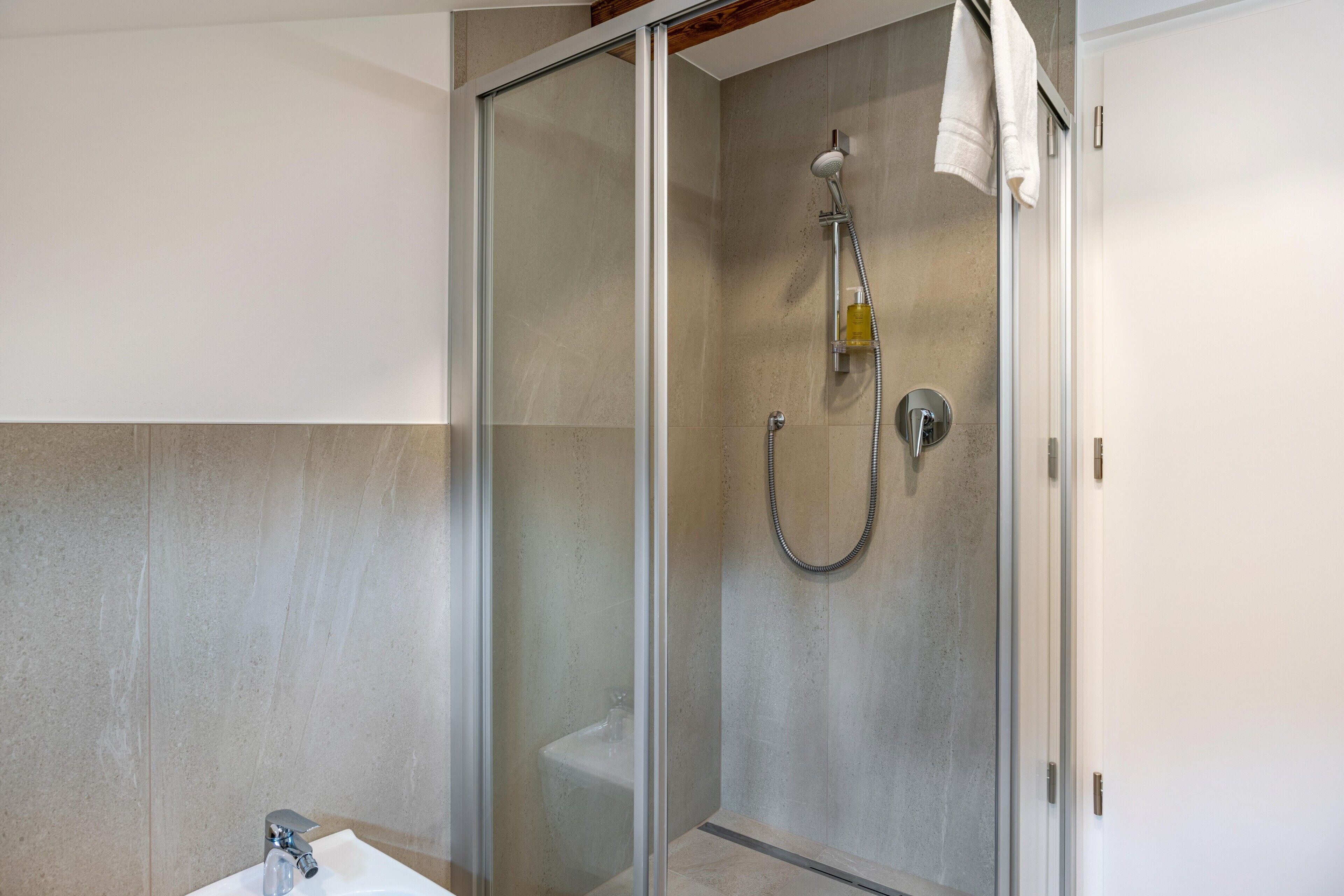 Un baño moderno con ducha de vidrio, un lavamanos blanco y una toalla colgada en la pared.