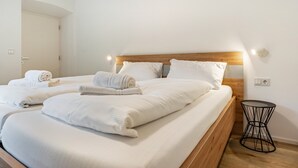 A hotel room with two beds, wooden headboards, white linens, a round black side table, and a white door. - Apartment '2' with Mountain View, Wi-Fi and Air Conditioning (Auer)