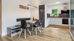 A modern kitchen with a dining area, featuring a wooden table, black chairs, and a built-in bookshelf. - Apartment '2' with Mountain View, Wi-Fi and Air Conditioning (Auer)