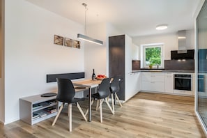 A modern kitchen with a dining area, featuring a wooden table, black chairs, and a built-in bookshelf.