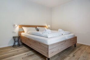 A modern bedroom with a wooden bed, white bedding, and a small black side table. - Apartment '2' with Mountain View, Wi-Fi and Air Conditioning (Auer)