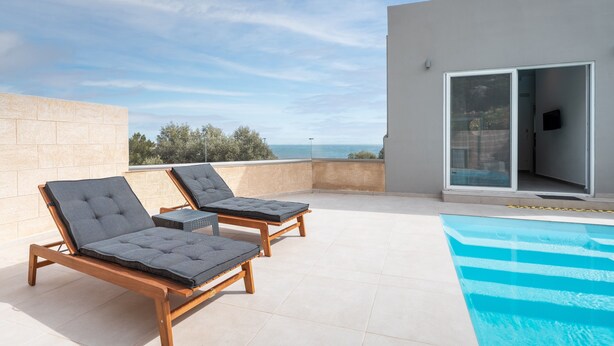 En tagterrasse med to liggestole, en swimmingpool og udsigt til havet.