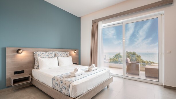 A bedroom with a large bed, a nightstand, a wooden headboard, a sliding glass door leading to a balcony, and a view of the sea. - Apartment 'Tesoro Del Mare with Sea View 1' with Sea View, Wi-Fi and Air Conditioning (Pefki)