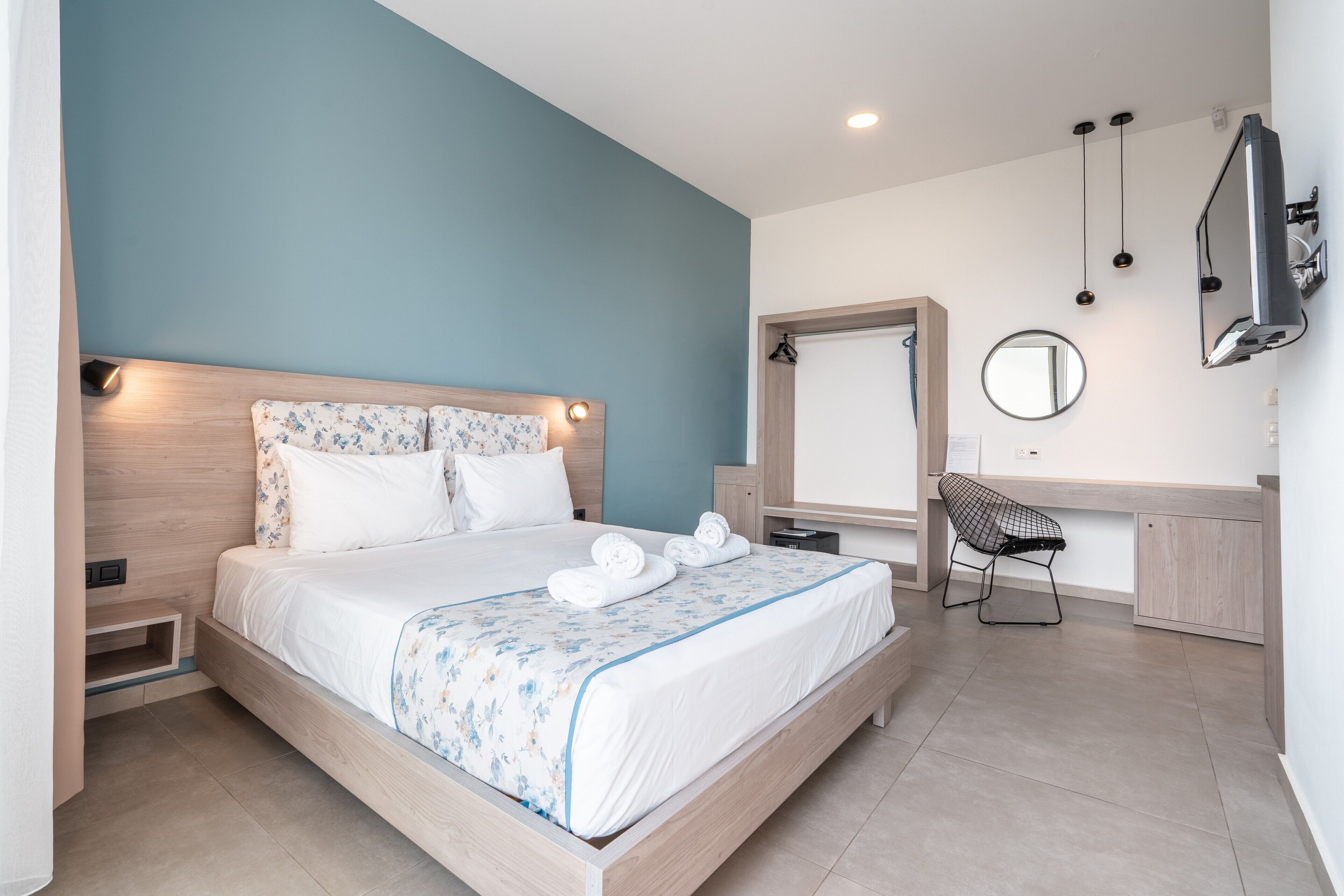A modern bedroom with a wooden bed, a desk, a chair, a mirror, and a TV.