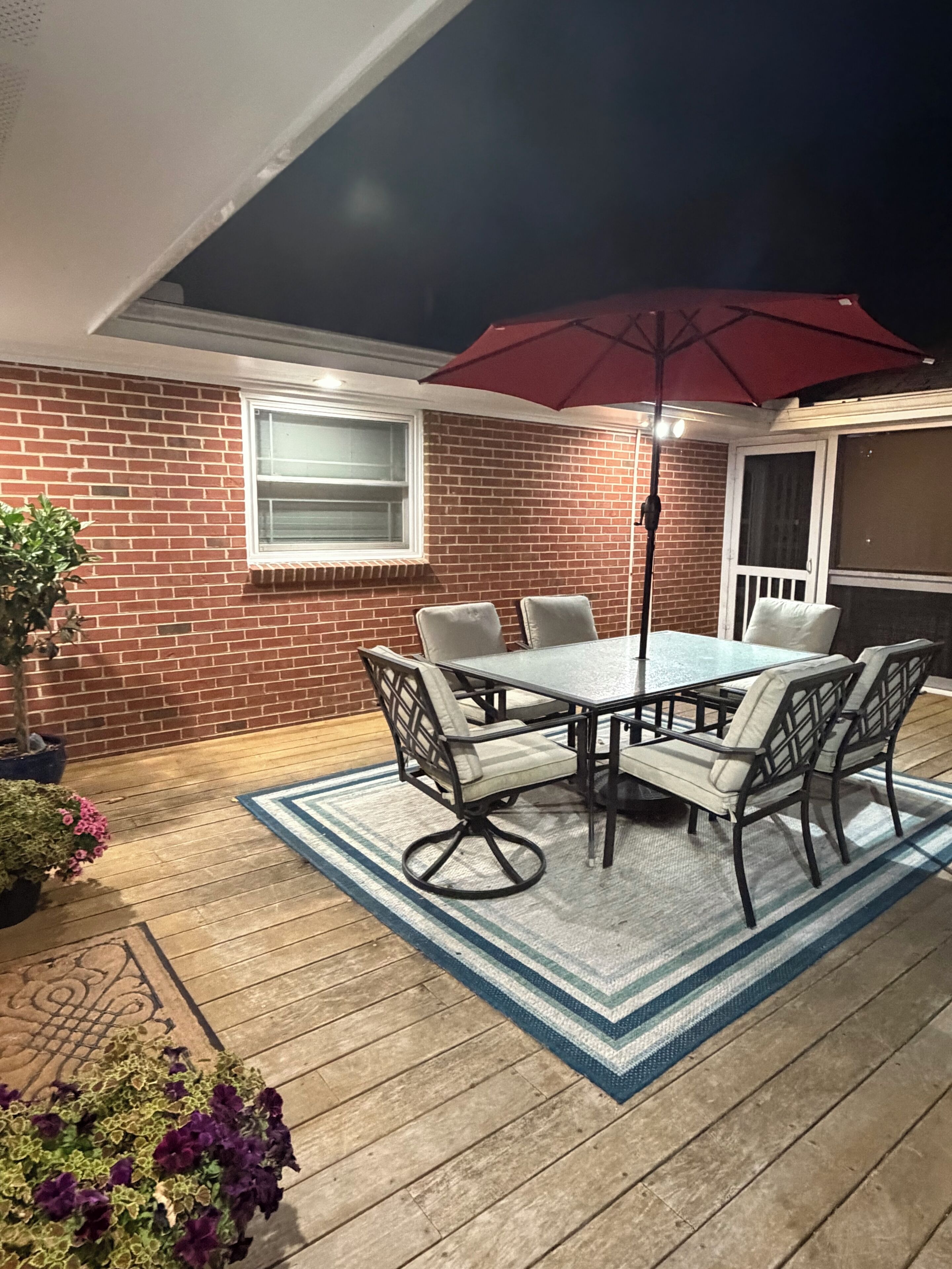 A patio with a table and chairs, a red umbrella, and potted plants.