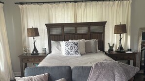 Un dormitorio con una cama grande, dos mesitas de noche, un ventilador de techo y un sofá gris con cojines.