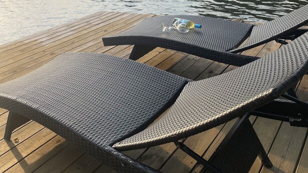Una terraza de madera con dos sillones de mimbre y una botella de vino.