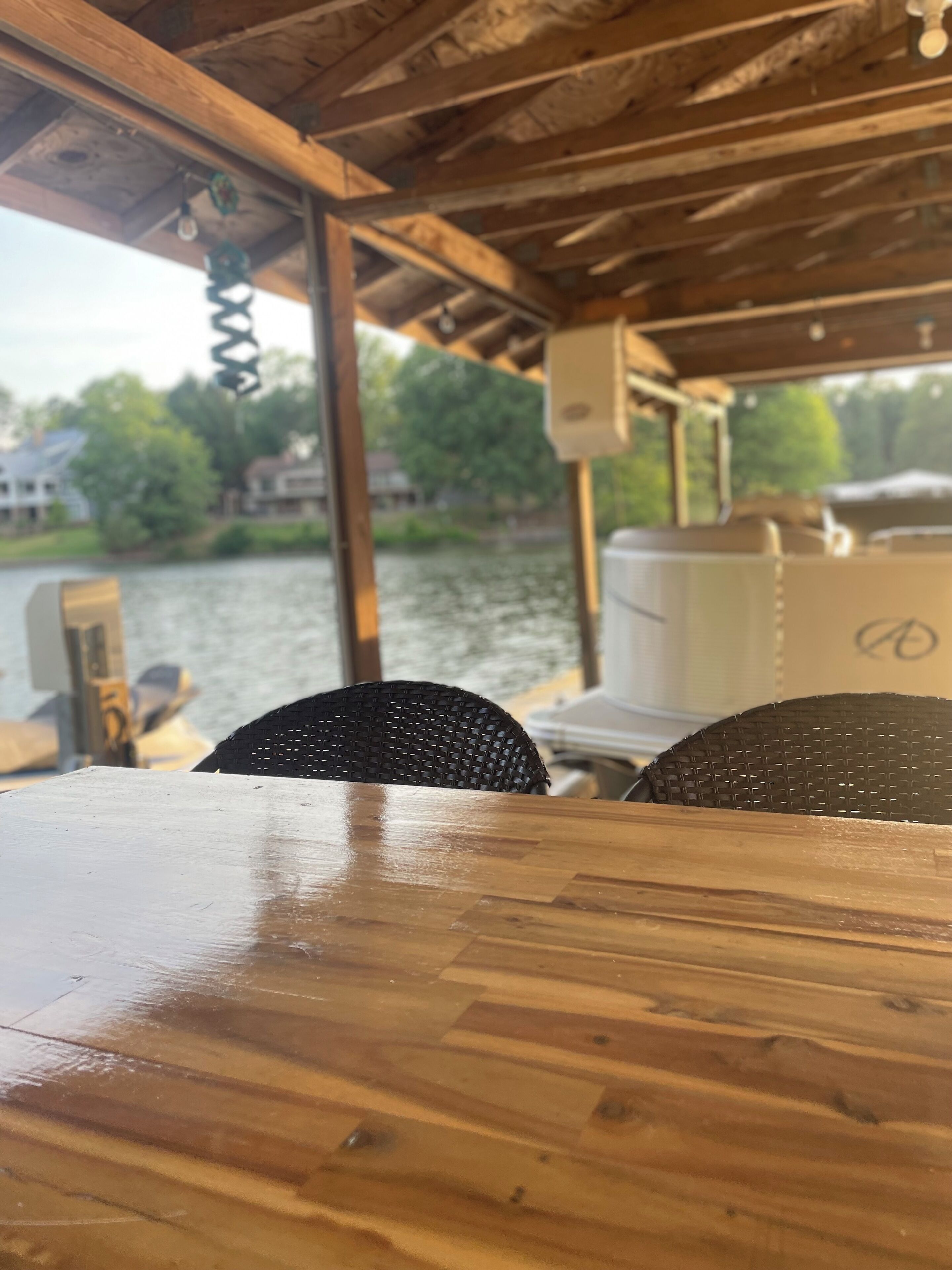A wooden table and chairs under a roofed area with a view of a river and houses in the background.