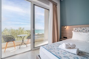 Une chambre d’hôtel avec un lit, une petite table, deux chaises, une table de chevet et une vue sur la mer, visible à travers une porte coulissante.