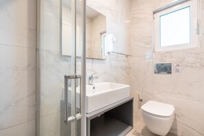 Une salle de bain avec un lavabo blanc, des toilettes et une cabine de douche en verre.