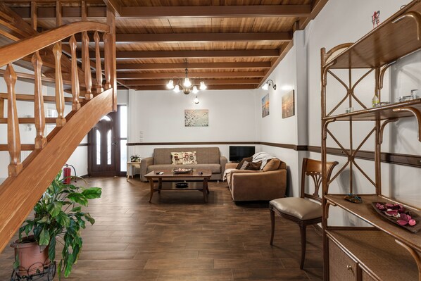 Una escalera de madera, una sala de estar con sofá, una mesa de centro, una televisión y una estantería.