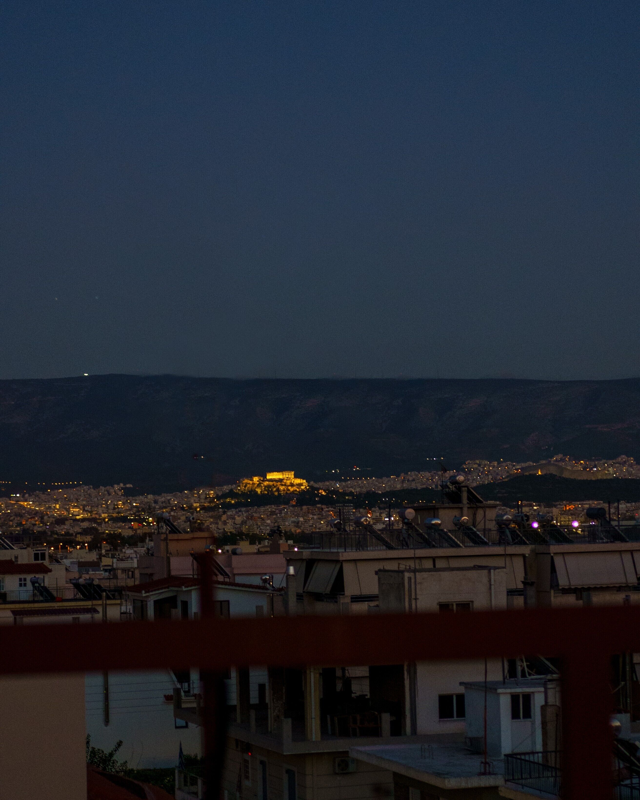 A cityscape at dusk with a prominent illuminated building in the distance.