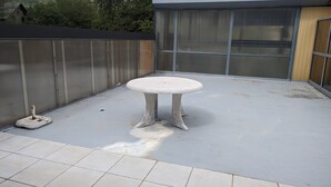A round table with a pedestal base on a flat surface, a metal fence, and a building with large windows in the background.