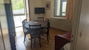 A dining area with a round table, chairs, a television, and a radiator.