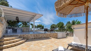 A stone patio with lounge chairs, a pergola, and a covered seating area.