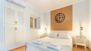 A bedroom with a bed, a wooden panel wall, a clock, and two bedside tables with lamps.