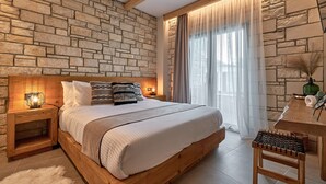 A bedroom with a stone wall, a wooden bed, a nightstand with a lamp, and a window with curtains. - Apartment 'Villa 2' with Mountain View, Balcony and Wi-Fi (Plati/Lasithi)