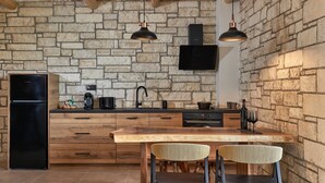 A kitchen with a stone wall, wooden cabinets, a black refrigerator, and a dining area with two chairs. - Apartment 'Villa 2' with Mountain View, Balcony and Wi-Fi (Plati/Lasithi)