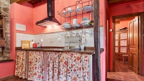 Una cocina con salpicadero de azulejos, un tendedero con vajilla, una encimera de madera y una cortina con estampado floral.