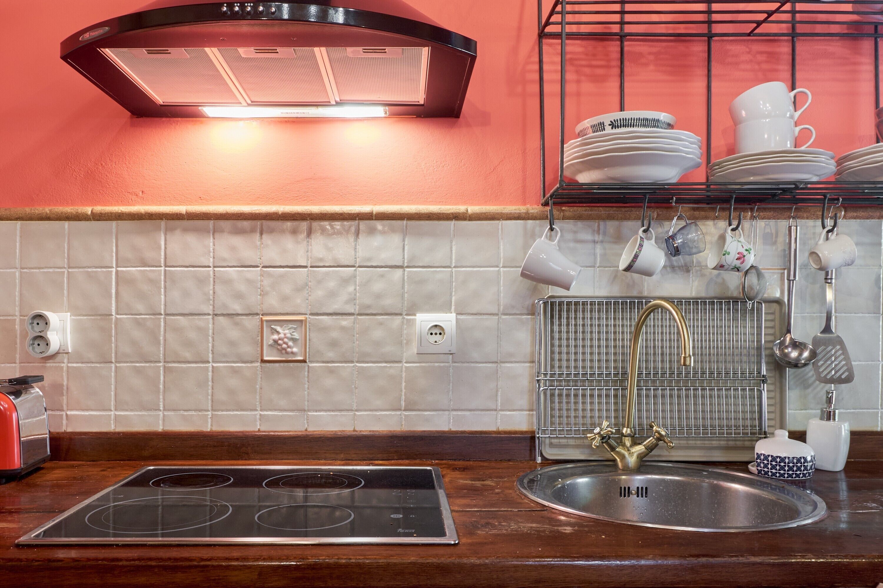 Una cocina con estufa a gas, un lavamanos con grifo dorado y una campana extractora.