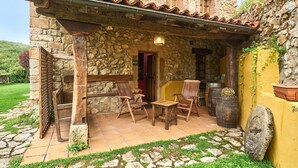 Un edificio de piedra con un patio empedrado, sillas de madera, una mesa y un farol.