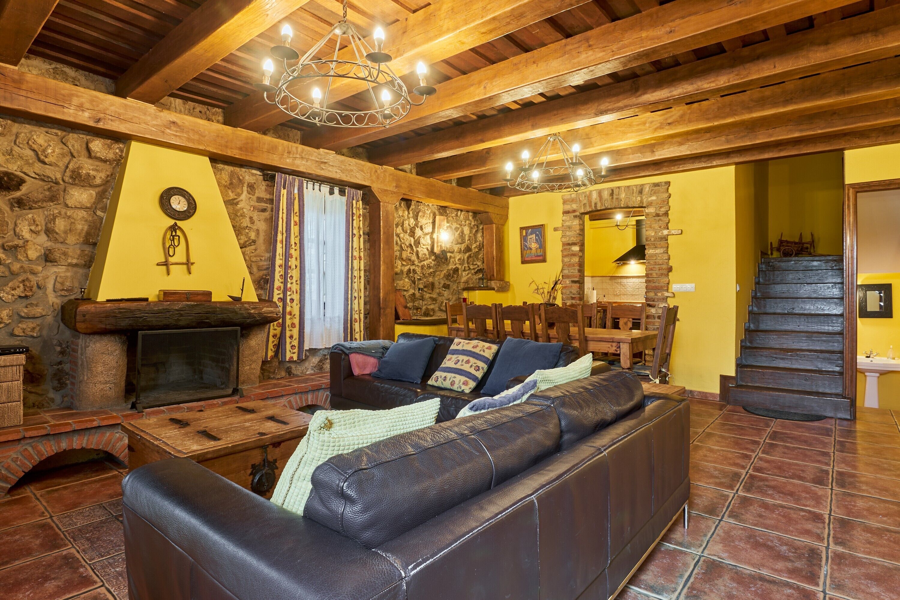 Um interior rústico com lareira de pedra, vigas de madeira, um sofá de couro e uma escada.